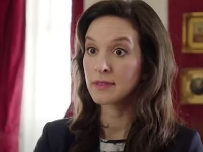 Louise Ford is wearing a black suit in the picture and is in a room that is red.